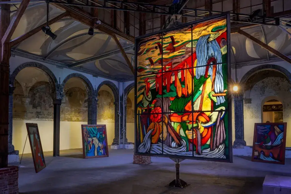 Vetrata colorata e quadri astratti in una sala con archi, un'installazione che ricorda l'arte di Ara Starck.