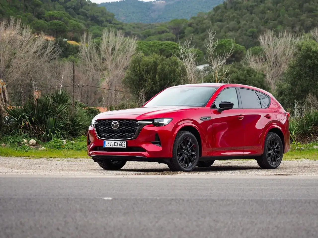 Czerwona Mazda CX-60 3.3 Diesel na tle zielonych wzgórz. Elegancka sylwetka i czarne felgi podkreślają jej sportowy charakter.
