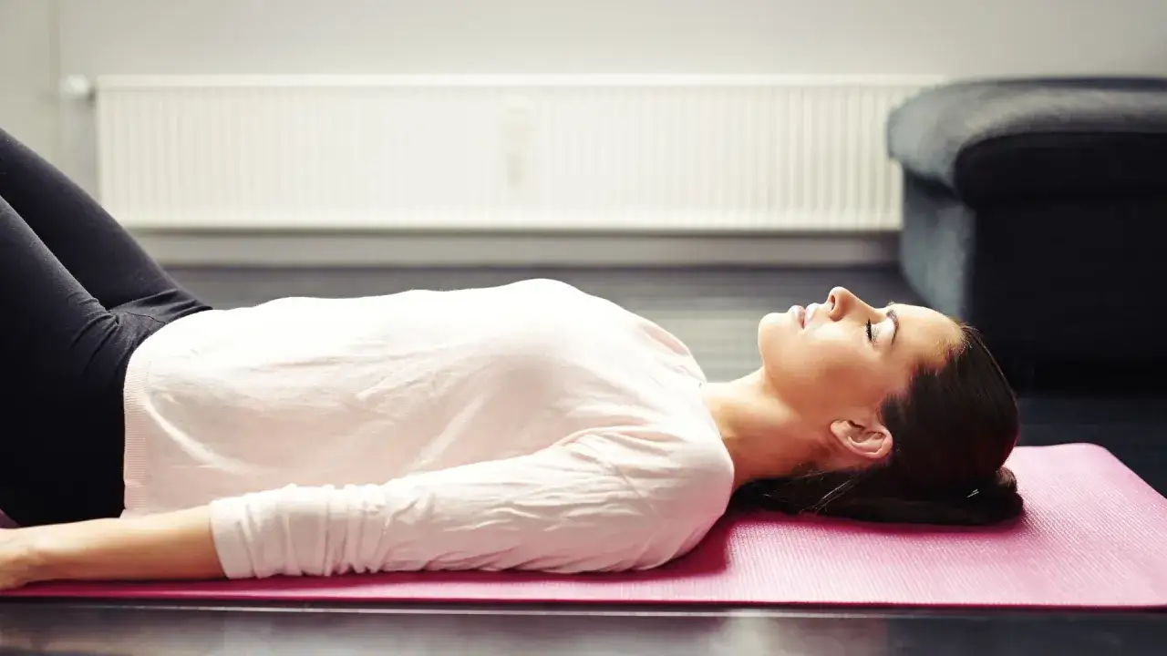 Kobieta w pozycji leżącej na macie, z zamkniętymi oczami, pogrążona w głębokim relaksie podczas sesji yoga nidra.