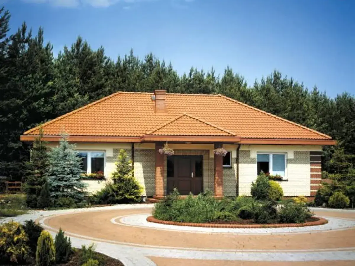 Elegancki ganek przed domem z czerwoną dachówką, otoczony zielenią i ozdobnym podjazdem.