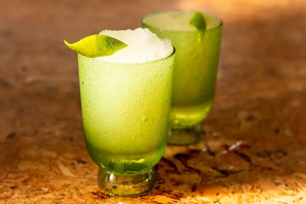 Zwei eisgekühlte Gin Tonic Drinks in grünen Gläsern, garniert mit Limettenschale, stehen auf einem Holztisch.