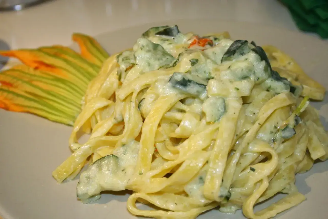 Un piatto invitante di pasta con fiori di zucca cremosa, guarnito con un fiore di zucca arancione.