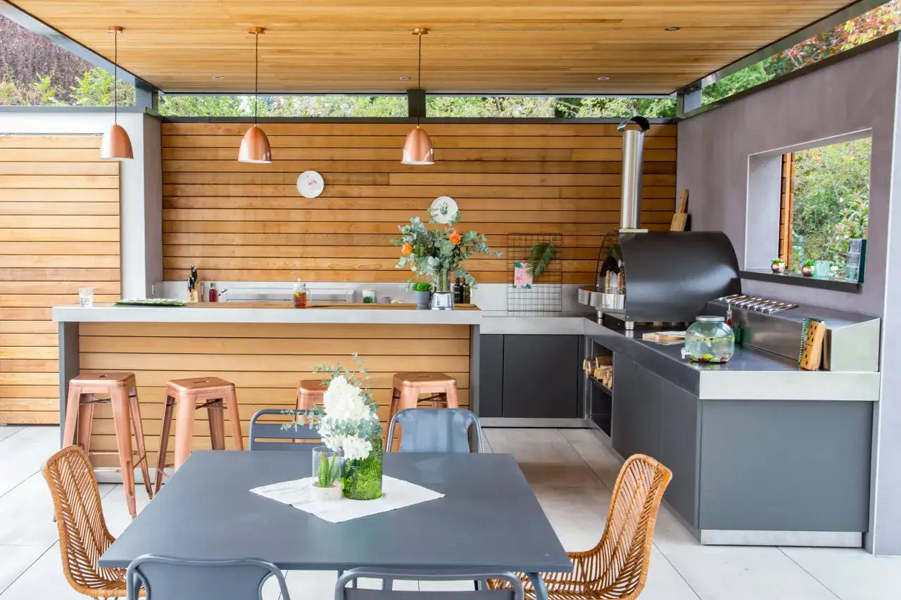 Un espace repas ext&eacute;rieur moderne avec un four &agrave; pizza, un bar et une table. Ce plan cuisine d'&eacute;t&eacute; est parfait pour recevoir.