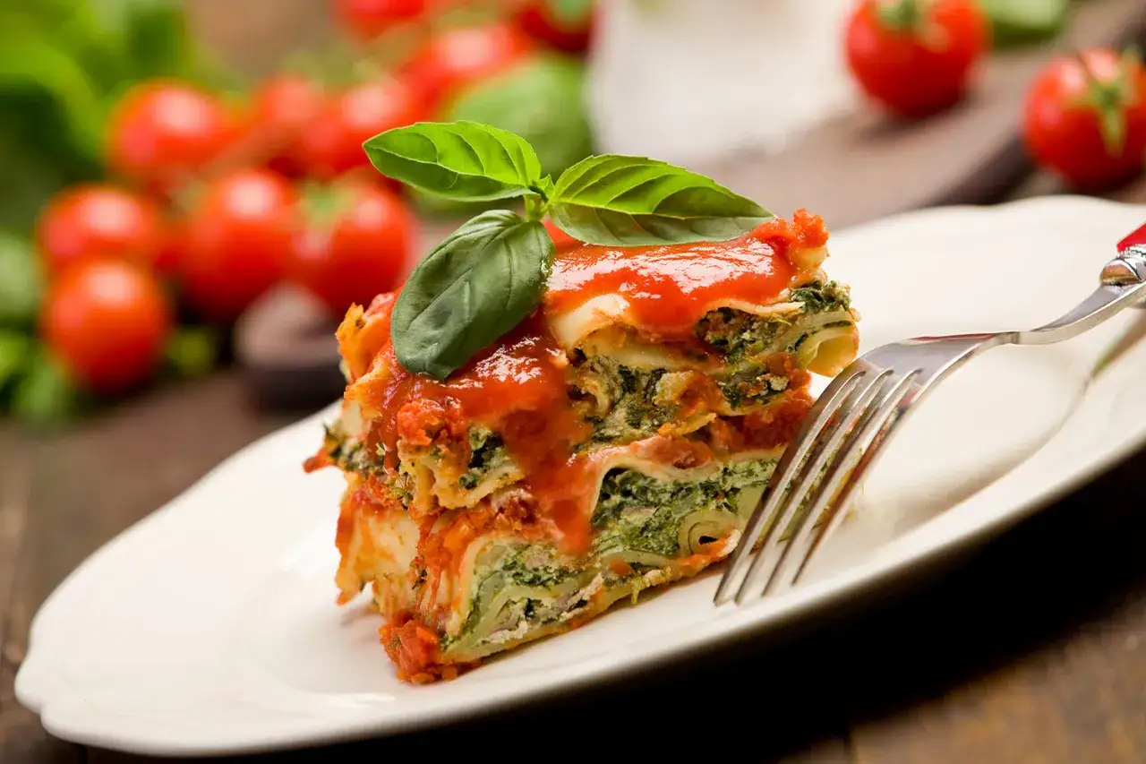 Pyszne lasagne z warzywami, polane sosem pomidorowym i udekorowane bazylią, na talerzu z widelcem.