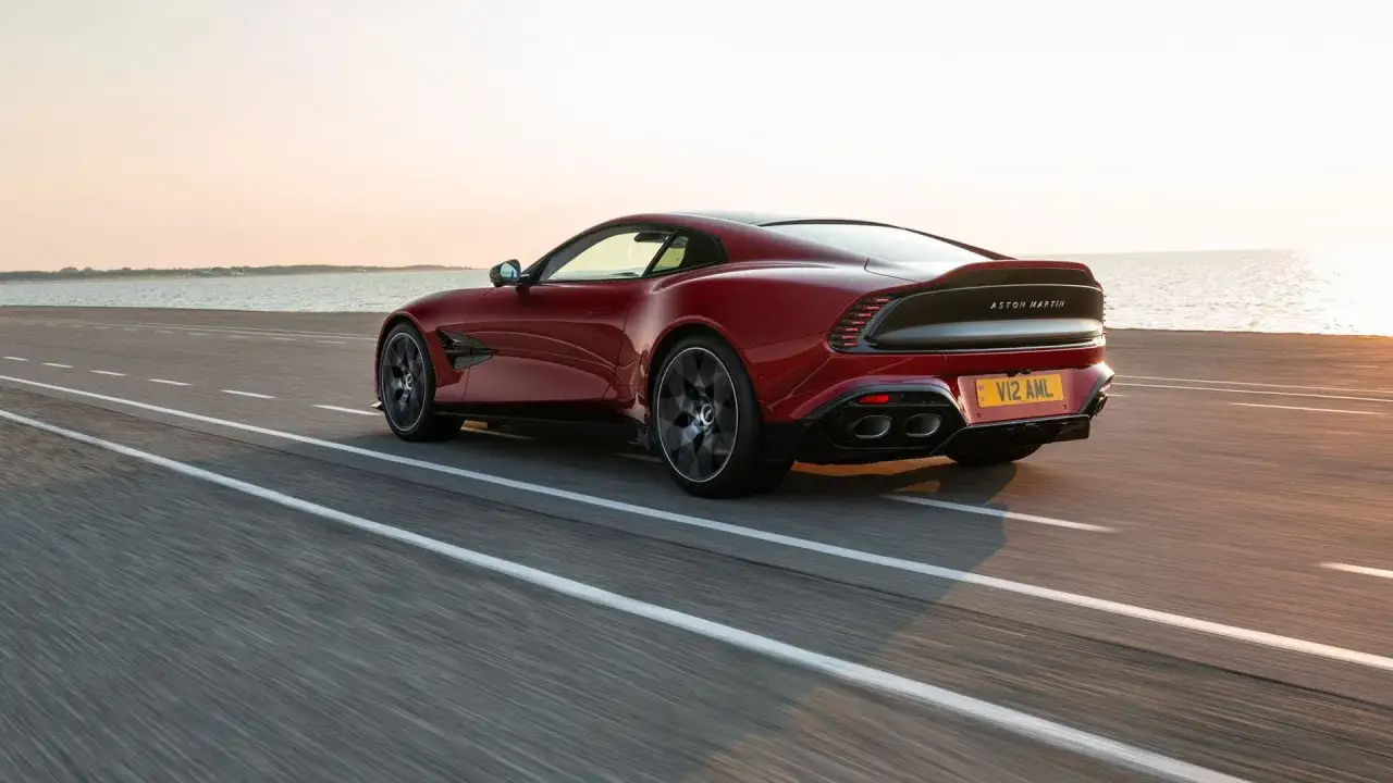 Czerwony Aston Martin Vanquish V12 AML pędzi wzdłuż wybrzeża o zachodzie słońca.