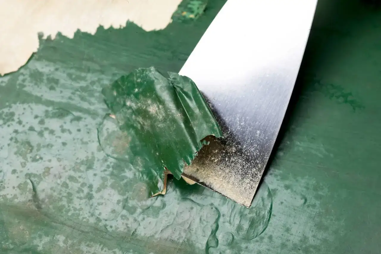 Esp&aacute;tula met&aacute;lica retirando pintura verde descascarada de una pared. Proceso de c&oacute;mo quitar pintura de la pared.