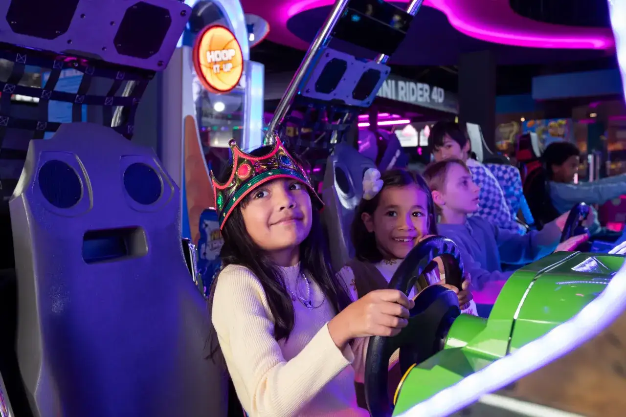 Kinder im Gamestate Potsdamer Platz, die begeistert Rennspiele spielen. Ein M&auml;dchen mit Krone am Steuer.