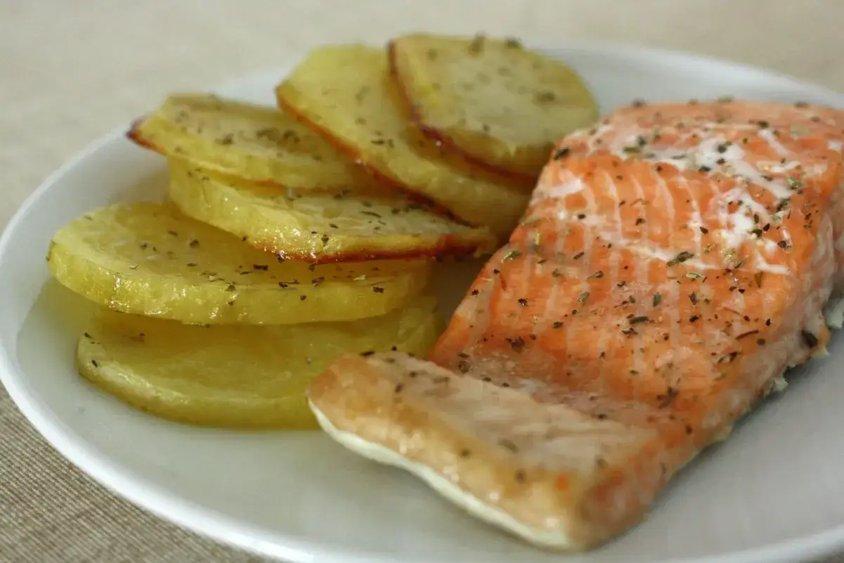 Un delicioso salmón al horno con patatas asadas, todo servido en un plato blanco.