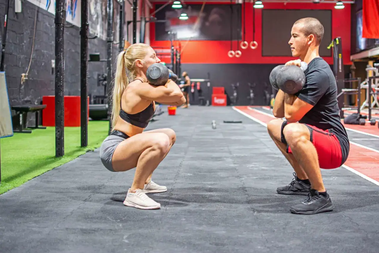 Eine mesomorphe Frau und ein Mann trainieren mit Kettlebells im Fitnessstudio.