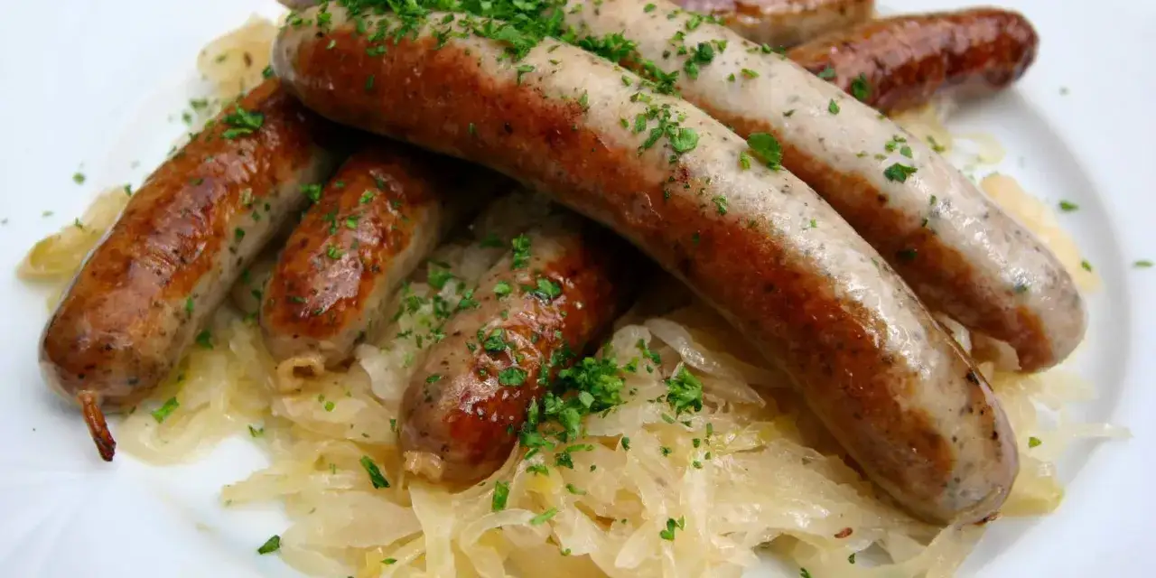 Salsicce dorate su un letto di crauti con aceto, guarnite con prezzemolo fresco. Un classico piatto che ricorda la ricetta crauti con aceto.