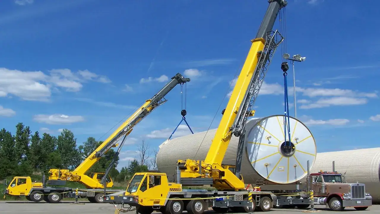 Dwa żółte dźwigi unoszą duży, cylindryczny element. To pokazuje, co to jest dźwig i jak potężne są te maszyny.