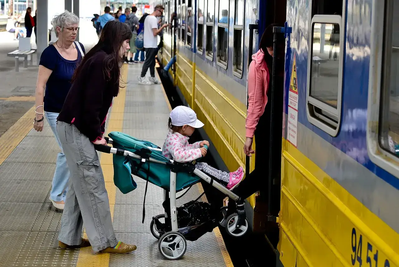Rodzina z wózkiem czeka na pociąg SKM w Sopocie. Dziecko w czapeczce siedzi w wózku, a kobiety przygotowują się do wejścia.