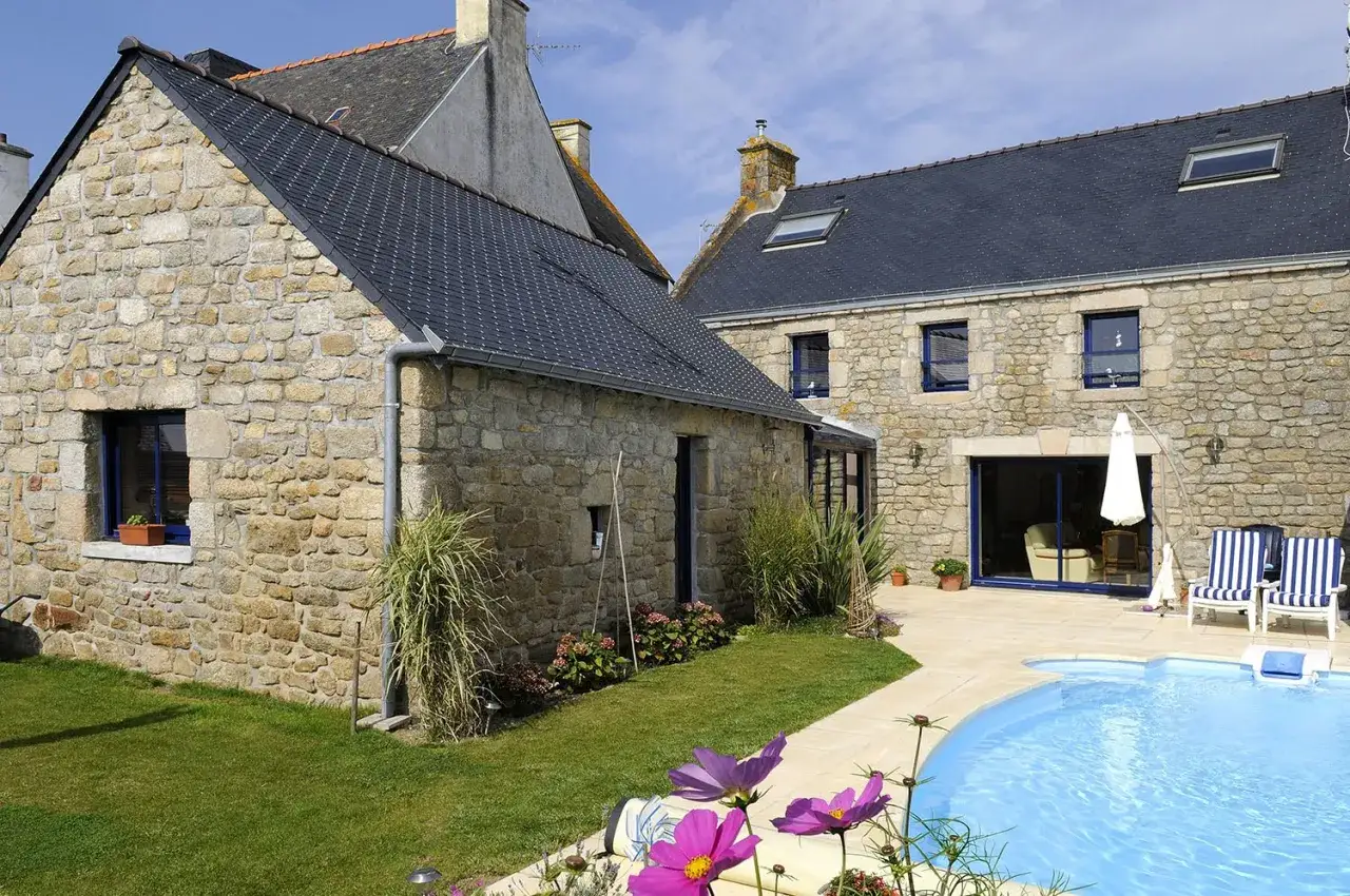 Belle maison en pierre calcaire avec piscine bleue et chaises rayées. Un jardin verdoyant entoure la propriété.