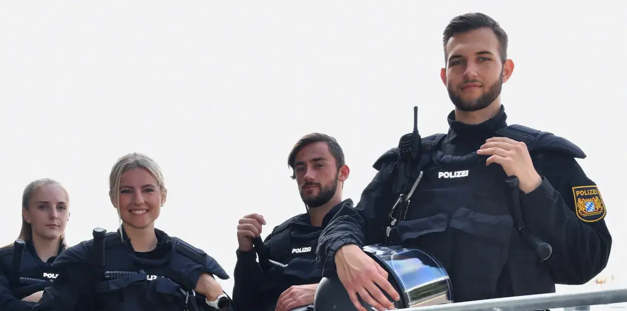 Vier Polizisten in voller Montur, die &uuml;ber ihre Ausr&uuml;stung und das gehobene Dienst Polizei Gehalt sprechen.