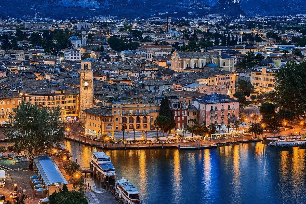 Riva del Garda cosa fare la sera: un panorama serale con il lago, le luci della citt&agrave; e il campanile illuminato.