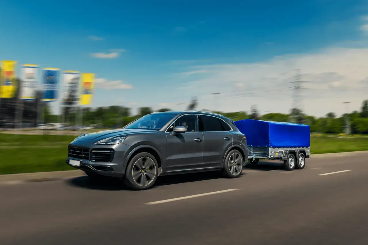 Szary SUV z przyczepką pod niebieską plandeką jedzie po drodze. Zastanawiasz się, ile można jechać z przyczepką?