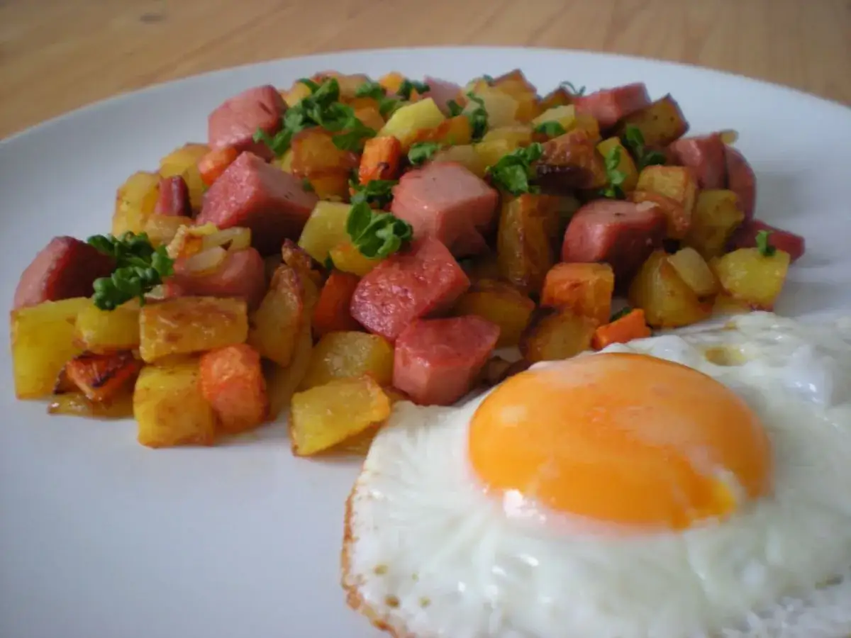 Pytt i panna: gebratene Kartoffelwürfel, Wurststücke und ein Spiegelei auf einem Teller.