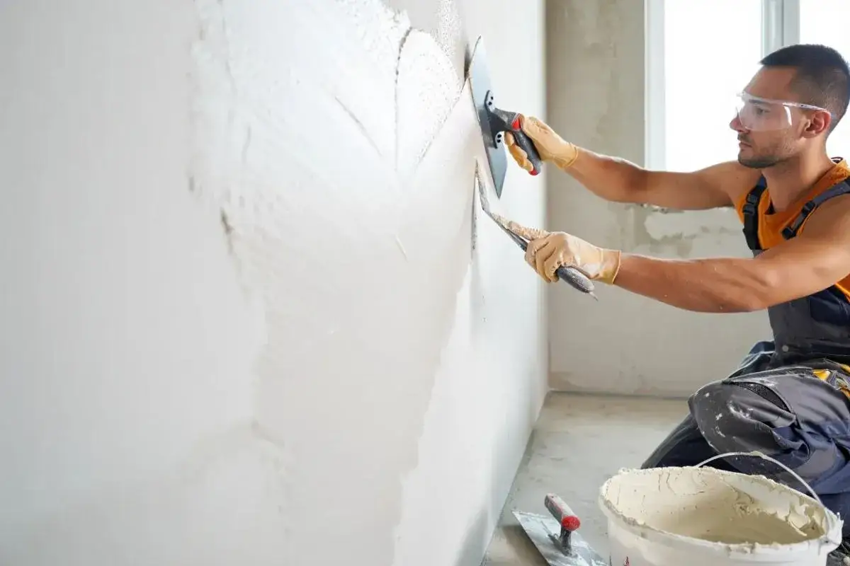 Un ouvrier applique un enduit sur un mur humide avec une taloche. Le travail progresse, laissant une surface lisse.