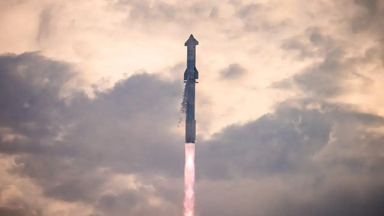 Starship startuje, wzbijając się w niebo na tle burzowych chmur. Płomienie silnik&oacute;w oświetlają niebo.
