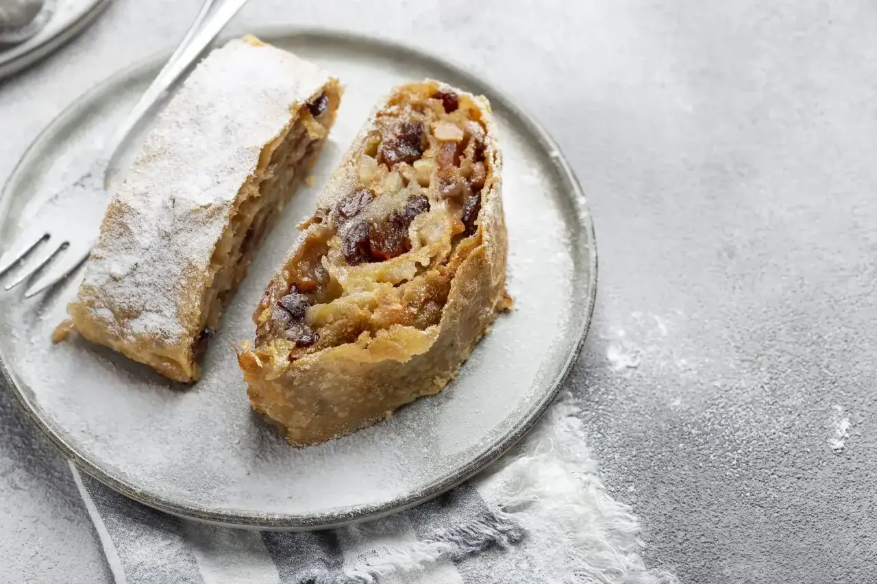 Due fette di strudel di mele, cosparse di zucchero a velo, su un piatto grigio.
