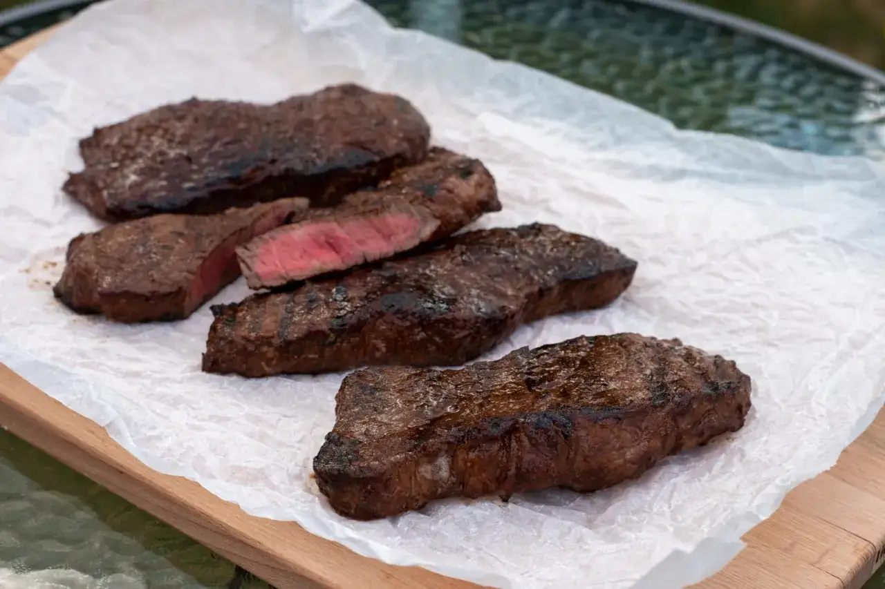 Grillad marinad ryggbiff, perfekt rosa i mitten, ligger p&aring; bakpl&aring;tspapper p&aring; en tr&auml;sk&auml;rbr&auml;da.