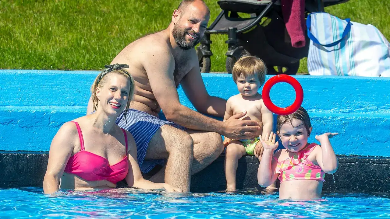 Familie genie&szlig;t den Sommer im Freibad Berlin. Ein fr&ouml;hliches Kind winkt, w&auml;hrend die Eltern und ein Baby entspannen.