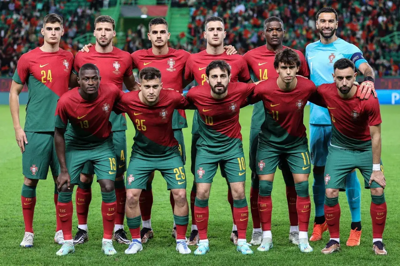 Drużyna piłkarzy Portugalii w czerwono-zielonych strojach pozuje do zdjęcia na boisku.