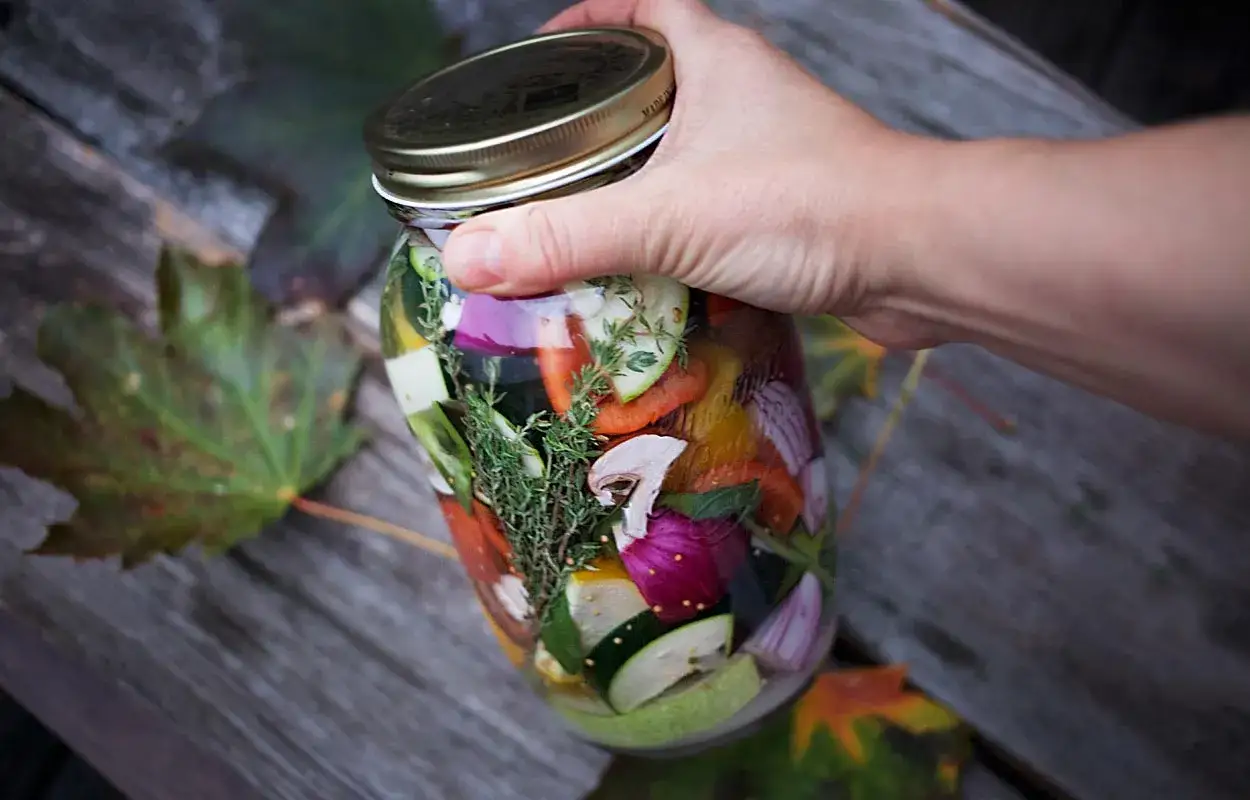 Hand schließt ein Glas mit bunten Gemüseschichten, bereit für mixed pickles selber machen.