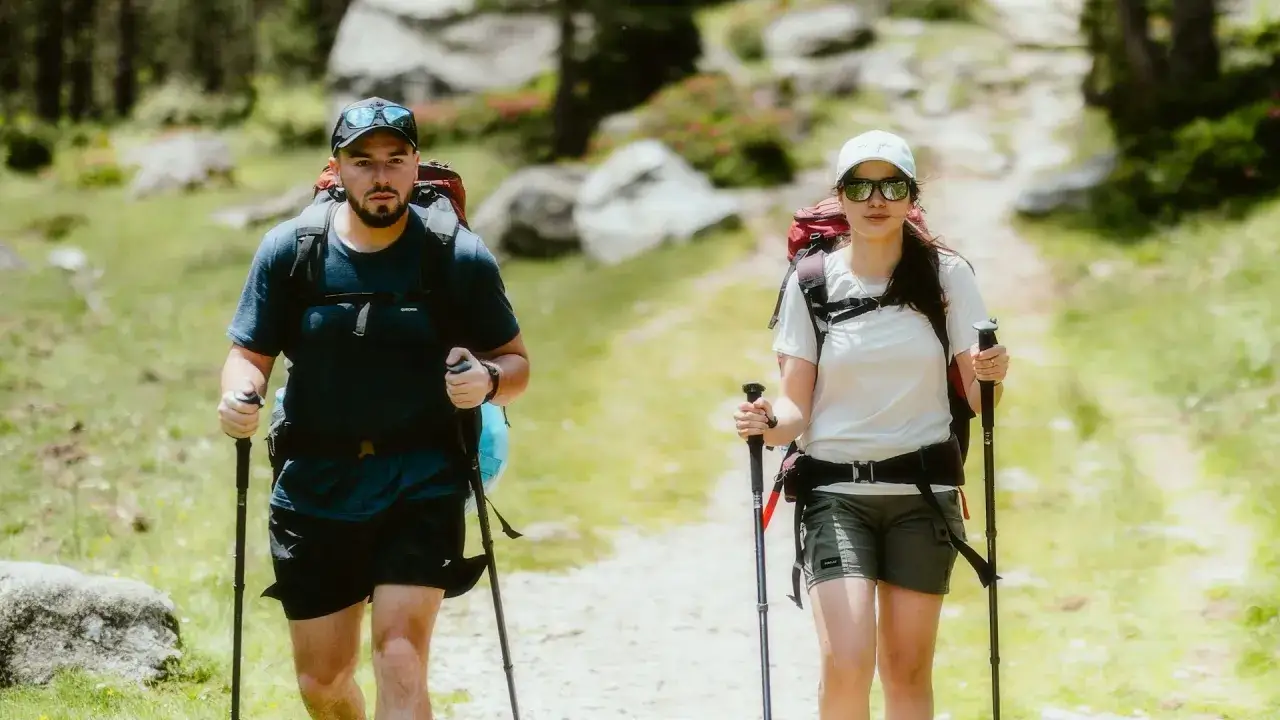 Co to jest nordic walking? Coppia con zaini e bastoncini cammina su sentiero in montagna, godendosi la natura.