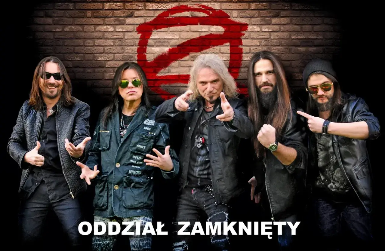 Pięciu rockmanów z zespołu Oddział Zamknięty, w skórzanych kurtkach, pozuje na tle ceglanej ściany z czerwonym znakiem zakazu.
