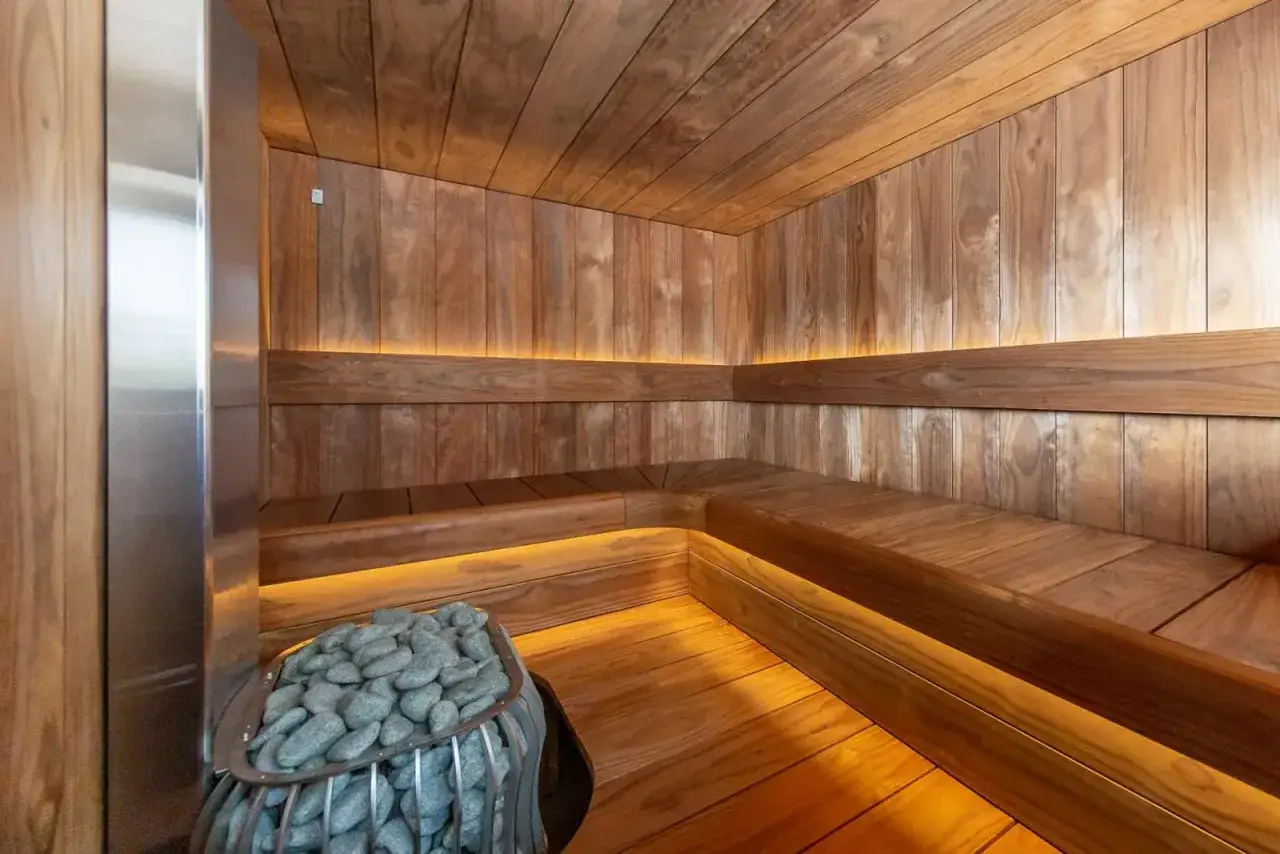 Drewniana sauna z kamiennym piecem i dyskretnym oświetleniem. Inspiracja, jak zbudować saunę marzeń.