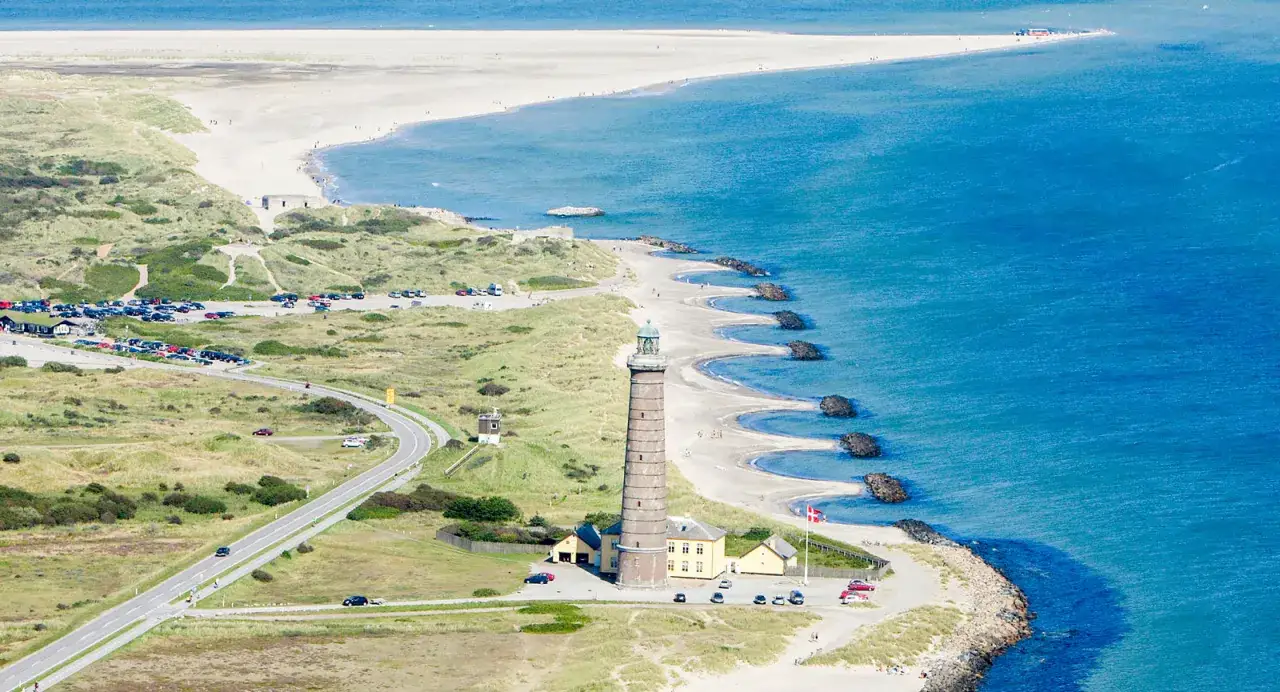 Skagens udde med sitt ikoniska fyr och böljande sanddyner, där vägen slingrar sig mot havet.