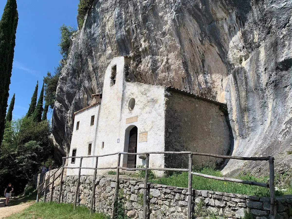 Piccolo eremo di San Valentino incastonato nella roccia, con un campanile a vela e un sentiero che conduce alla sua porta.