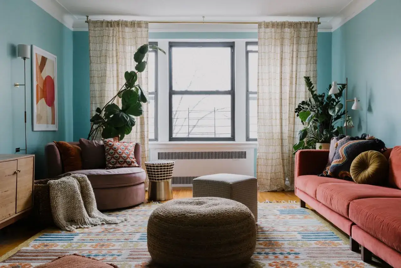 Salón con sofá coral, sillón rosa, alfombra geométrica y plantas. Un espacio acogedor con un **diseño aesthetic** que invita a la relajación.