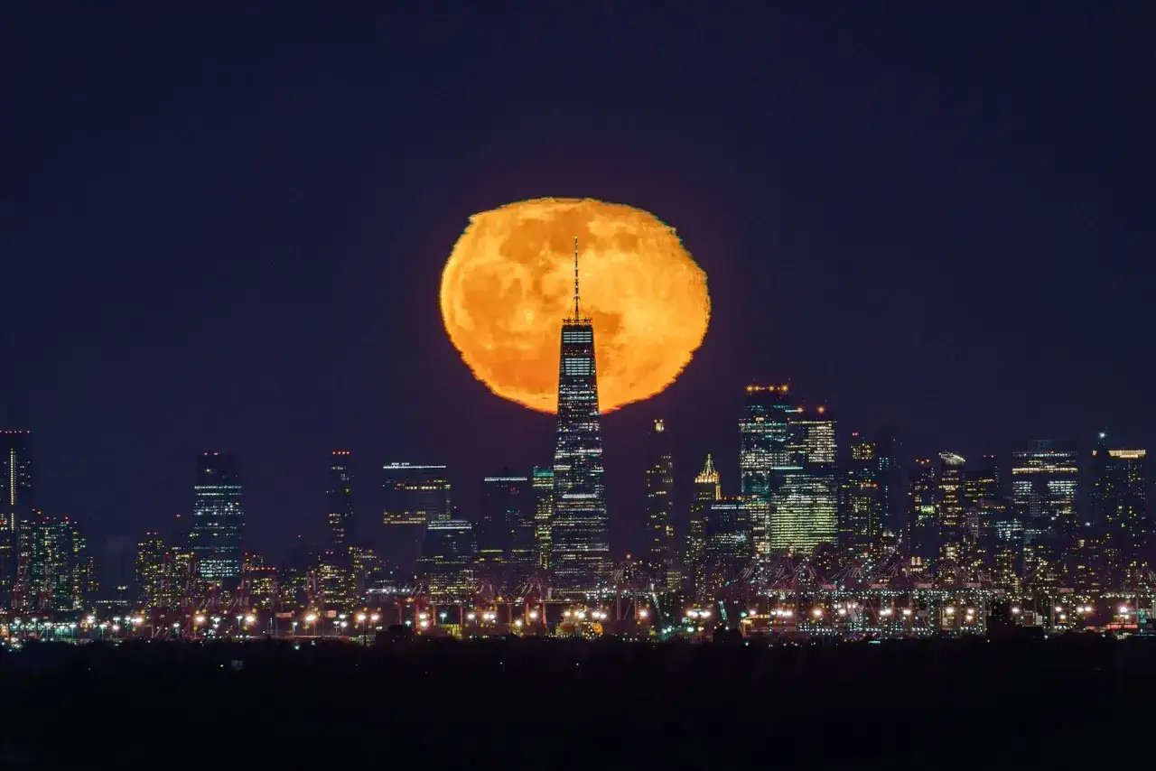 Pomarańczowe zdjęcie księżyca w pełni nad Nowym Jorkiem, zdominowane przez wieżowiec One World Trade Center.