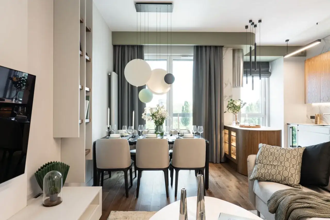 Elegancka jadalnia z nowoczesnym oświetleniem i akcentami w kolorze pistacjowym. Stół nakryty do kolacji, obok wygodna sofa.