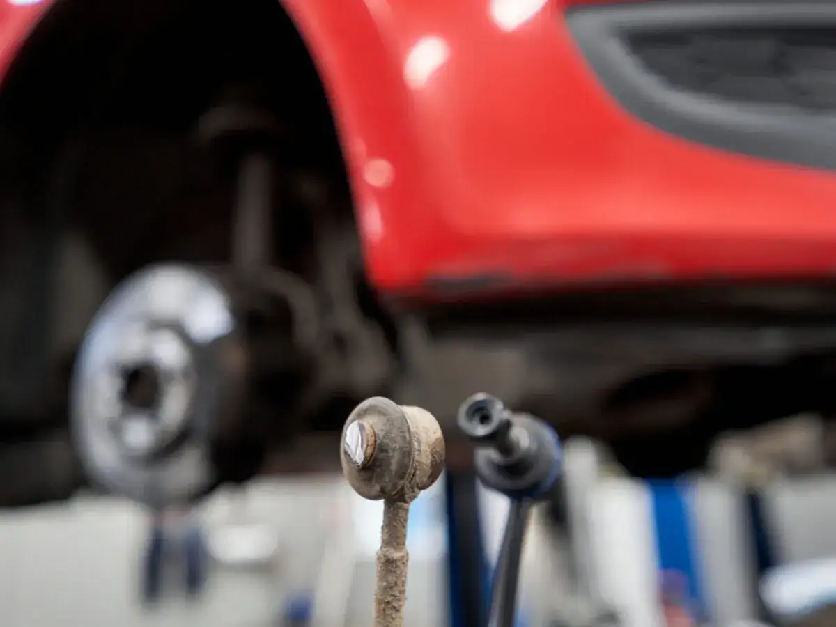 Zwei Koppelstangen liegen vor einem roten Auto. Eine ist offensichtlich defekt und muss ersetzt werden.