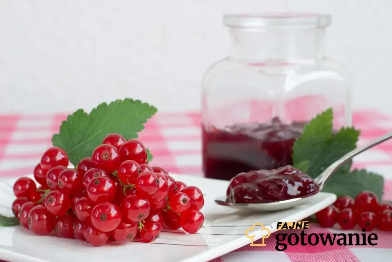 Pyszny dżem z porzeczki czerwonej na łyżeczce, obok świeże owoce i słoiczek domowego przetworu.