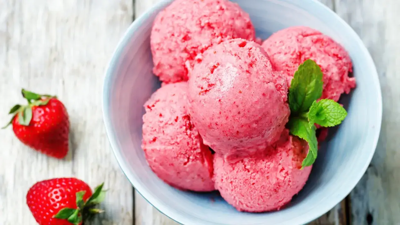 Schüssel mit erfrischendem Erdbeereis mit Sahne, garniert mit Minze. Daneben liegen frische Erdbeeren.