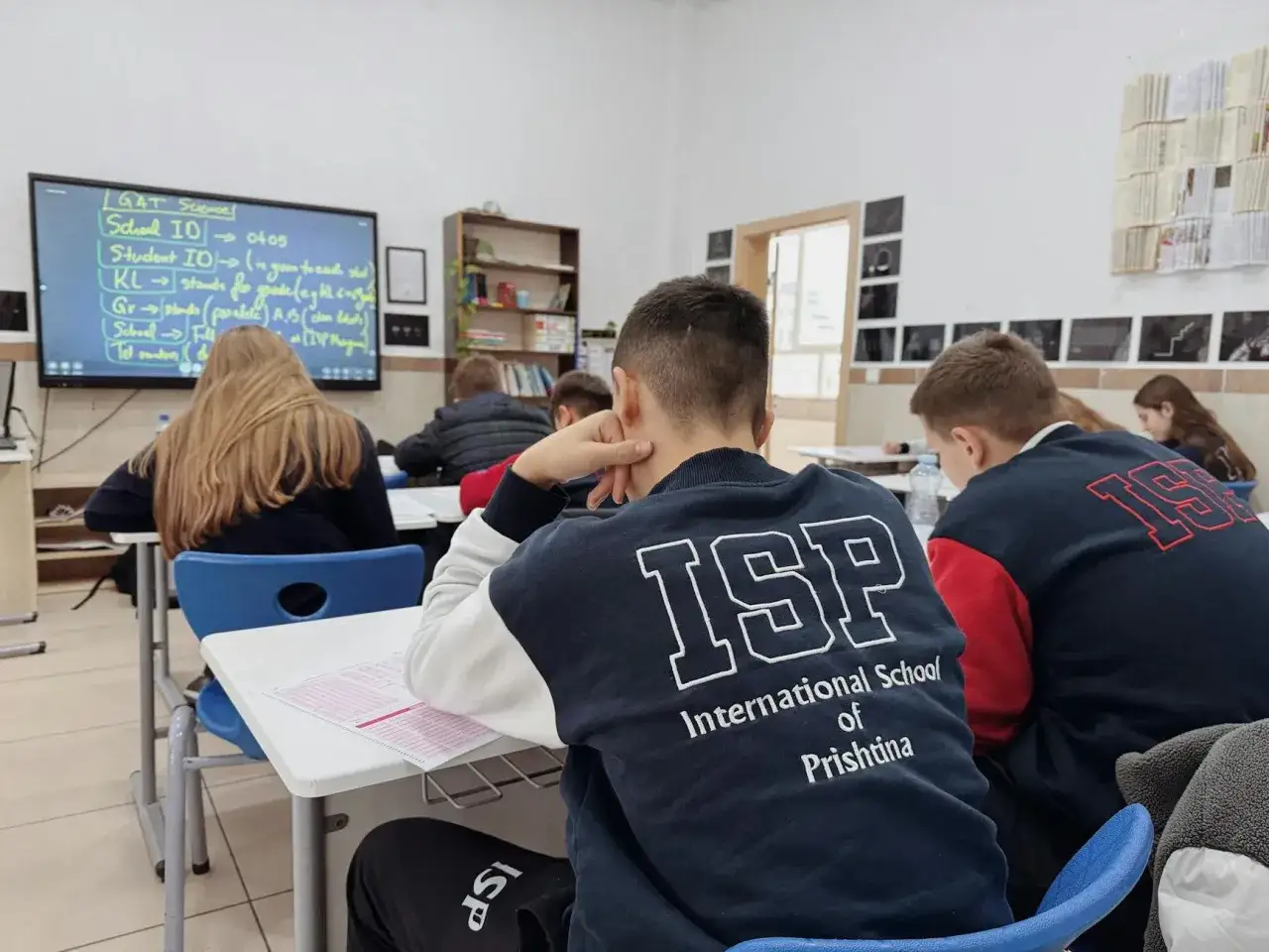 Uczniowie w klasie International School of Prishtina, skupieni na lekcji. Na ekranie widać notatki dotyczące