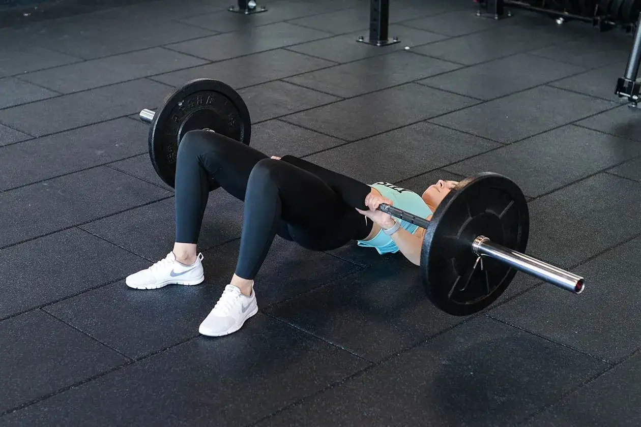 Kobieta wykonuje hip thrust po polsku z obciążeniem na biodrach. Ćwiczenie na siłowni.