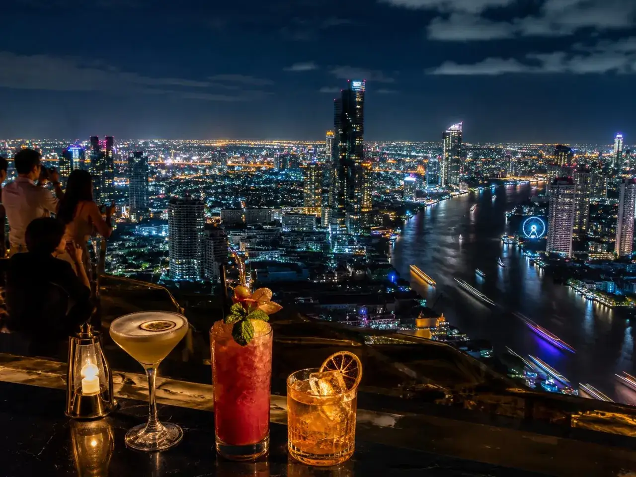 Cocktails sur un rooftop à Bangkok, avec vue sur la ville illuminée et le fleuve la nuit.