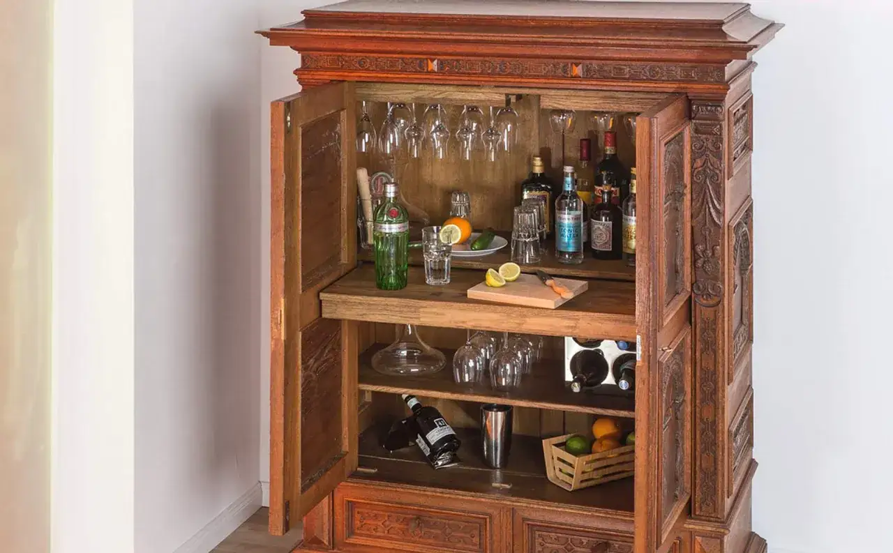 Ein antiker Schrank, der sich perfekt zum **bar selber bauen** eignet. Gef&uuml;llt mit Flaschen, Gl&auml;sern und Fr&uuml;chten, bereit f&uuml;r den n&auml;chsten Drink.