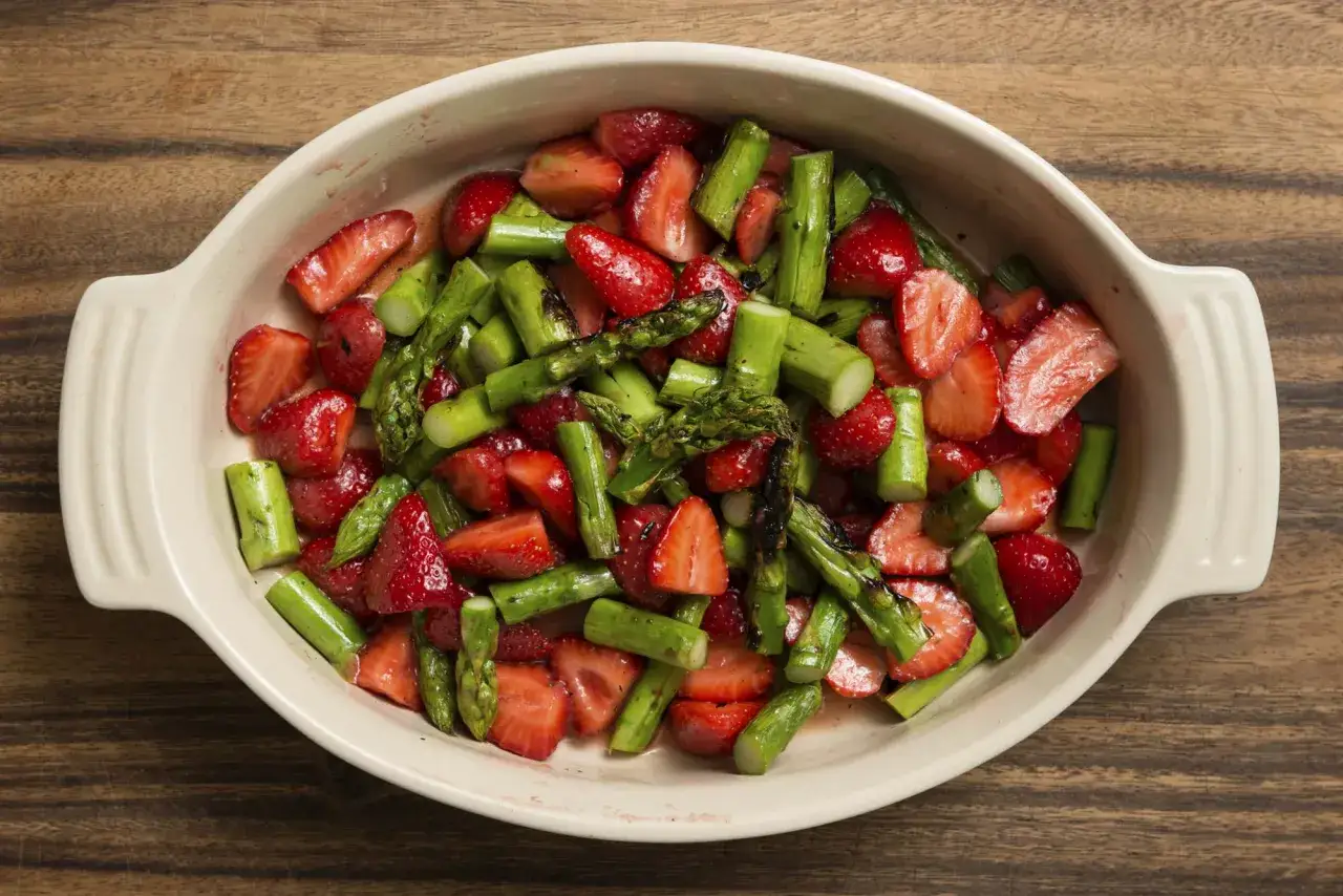 Ein frischer Spargelsalat mit Erdbeeren in einer cremefarbenen Schale auf Holzuntergrund.