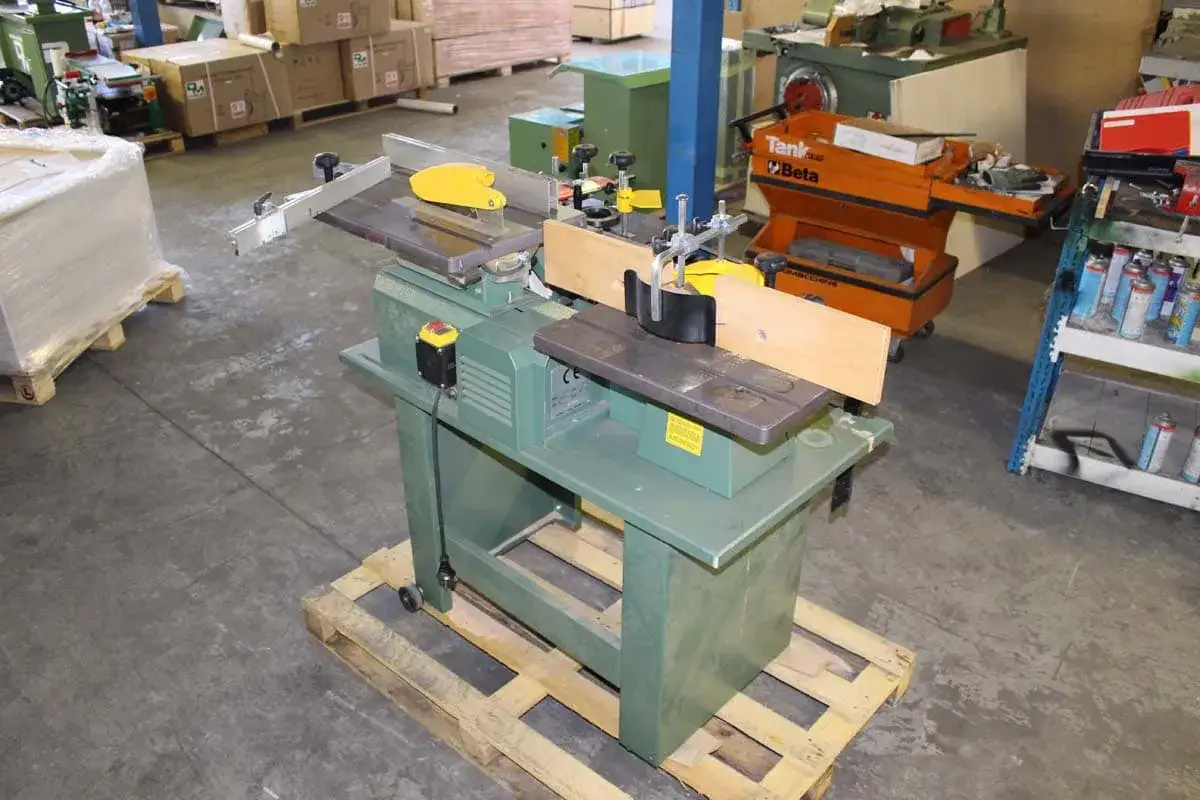 Machine &agrave; bois verte, une scie kity, avec des outils et des bo&icirc;tes en arri&egrave;re-plan.
