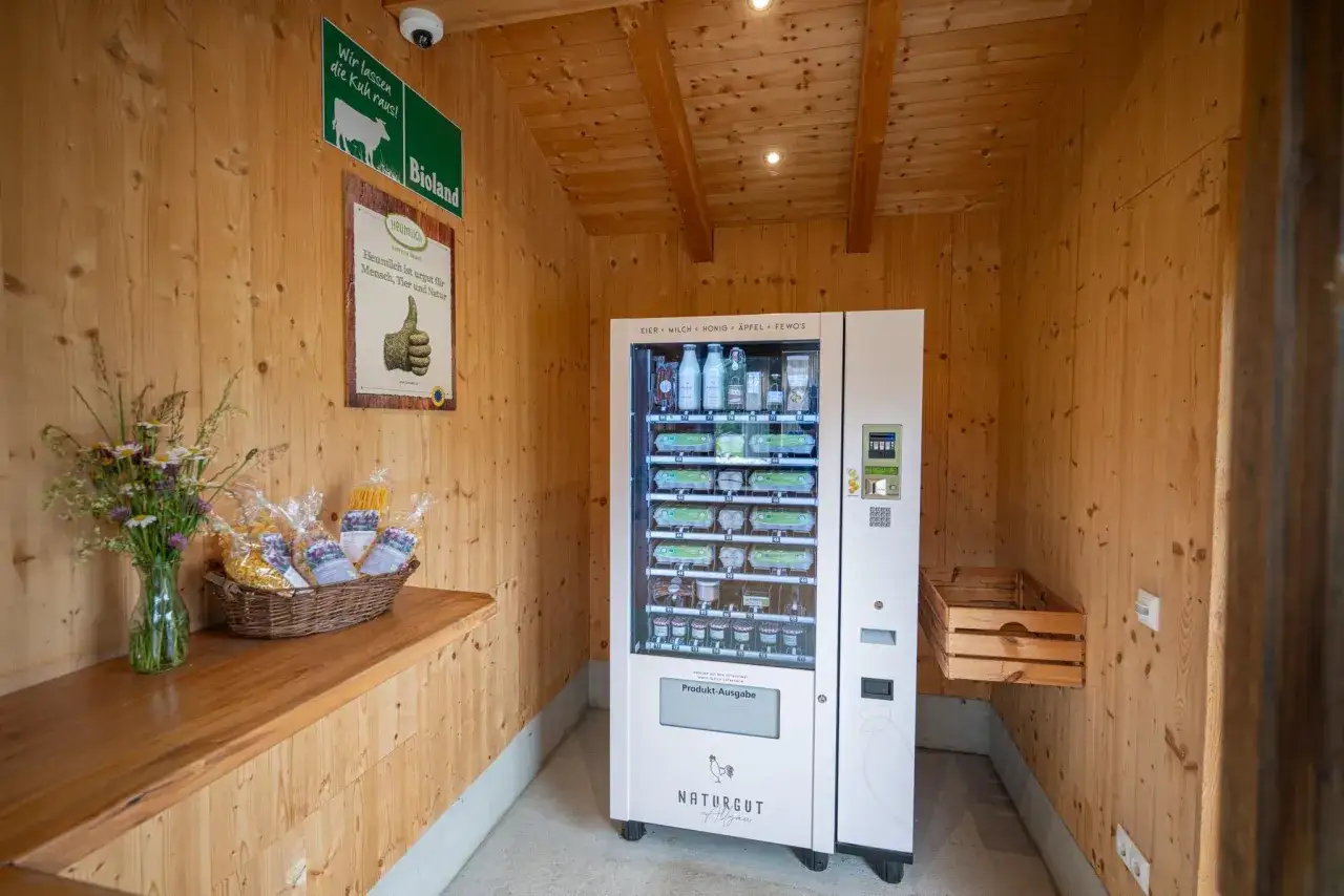 Selbstbedienungsautomat mit Eiern, Milch und Honig. Ein Korb mit Nudeln und Blumen steht daneben.