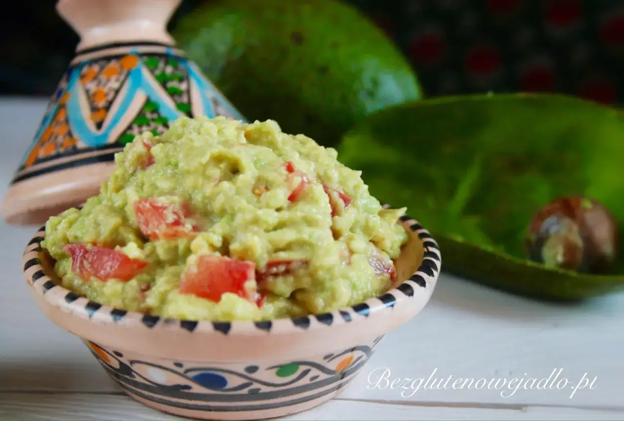 Pyszne guacamole co to? Kremowy dip z awokado i pomidorów w ozdobnej miseczce, z awokado w tle.