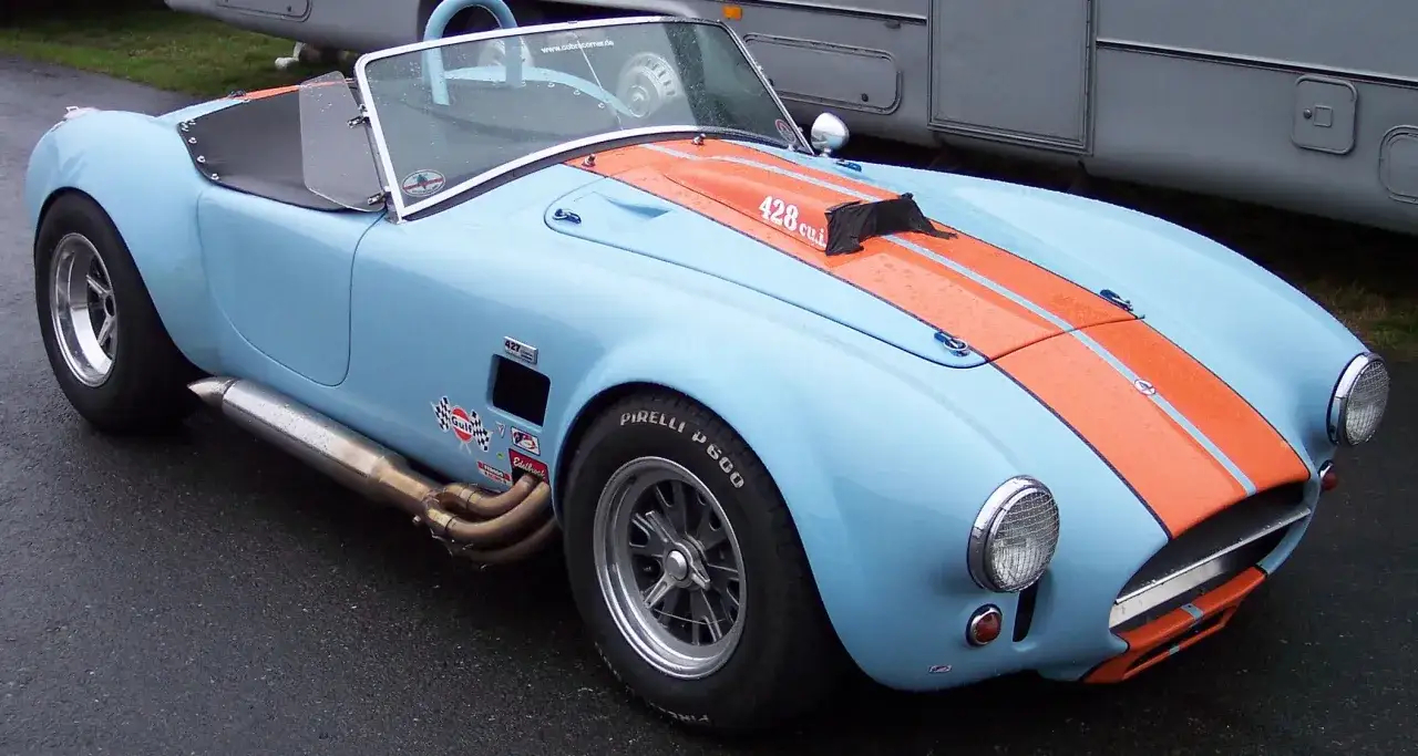 Hellblauer Shelby Cobra 427 mit orangen Streifen und Auspuffrohren, bereit für die Rennstrecke.