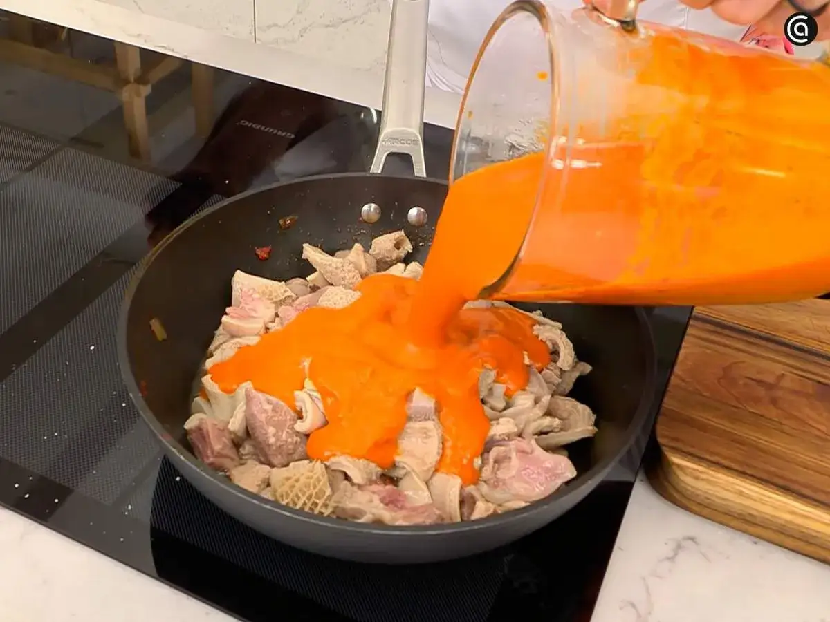 Se vierte salsa roja sobre trozos de callos en una sart&eacute;n, preparando unos deliciosos callos a la vizcaina.