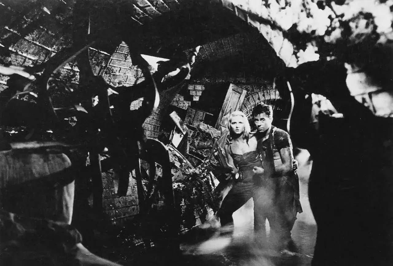 Para zniszczonego wnętrza, jak z polskich filmów z lat 50, 60, 70. Mężczyzna obejmuje kobietę, oboje wyglądają na zaniepokojonych.